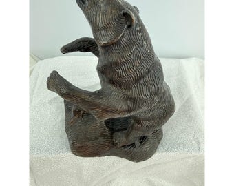 May include: A bronze-colored bear sculpture in a standing pose, with its head raised and mouth open. The bear's fur is detailed with textured lines, and its paws are extended. The sculpture is mounted on a rectangular base.