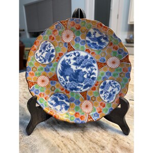 May include: A round ceramic plate with a scalloped edge featuring a central blue and white lion motif surrounded by floral patterns. The background displays a colorful honeycomb grid in green, orange, and blue, interspersed with circular medallions.