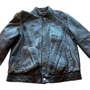 May include: A vintage, dark brown leather jacket with a zip-up front and two front pockets. The jacket features a ribbed hem and cuffs, and decorative stitching on the shoulders and sleeves. The jacket has a classic, bomber-style design.