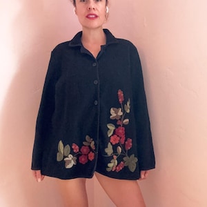 May include: Black button-down jacket with floral embroidery in red, green, and tan. The jacket has a collar and long sleeves. The floral design is on the lower right side of the jacket.
