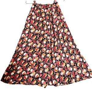 May include: A long, floral skirt with a black background and a pattern of pink, white, and yellow flowers. The skirt is buttoned down the front and hangs from a hanger. The fabric appears to be lightweight and flowing.