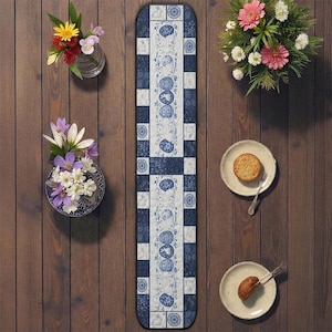 Könnte beinhalten: Ein blau-weiß gemusterter Tischläufer mit floralem Design, der auf einem Holztisch platziert ist. Der Läufer ist umgeben von kleinen Tellern mit Gebäck, Vasen mit Blumen und einem Strauß rosa und weißer Blumen.