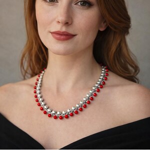 Può includere: Una collana argentata e rossa con un design gotico medievale. La collana presenta perline argentate e perline rosse vivaci alternate, creando un contrasto sorprendente. La collana è indossata da una persona con i capelli rossi e un top nero.