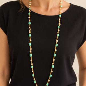 Può includere: Una collana lunga con un cordino giallo vivace infilato con un'alternanza di perline rettangolari color turchese e piccole perline biancastre, pallide e traslucide, che creano un motivo continuo lungo l'intera lunghezza del gioiello.