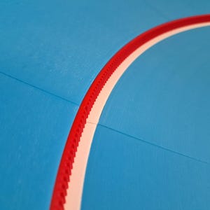 May include: Close-up of a blue surface with a curved red and white border. The red border has a ridged texture. A yellow shape is visible in the corner. The image has a smooth, matte finish.