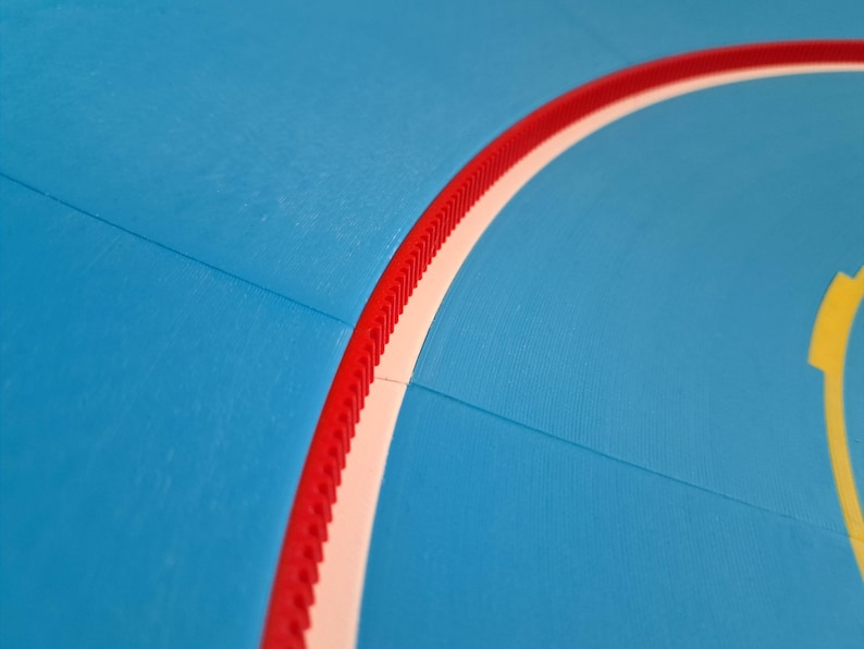 May include: Close-up of a blue surface with a curved red and white border. The red border has a ridged texture. A yellow shape is visible in the corner. The image has a smooth, matte finish.