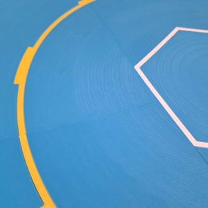 May include: Close-up of a blue surface with a textured pattern. A yellow curved line with rectangular breaks and a white hexagon outline are visible. The image has a modern, abstract design.