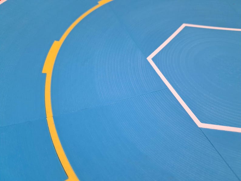 May include: Close-up of a blue surface with a textured pattern. A yellow curved line with rectangular breaks and a white hexagon outline are visible. The image has a modern, abstract design.