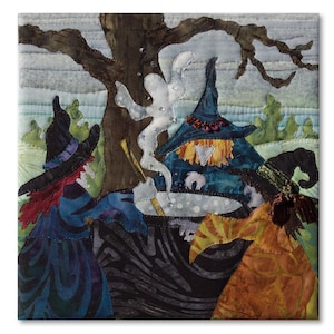 May include: A fabric wall hanging featuring a quilted scene of three figures in pointed hats gathered around a black cauldron. A white ghost rises from the pot, set against a dark tree and a pale sky. The scene uses layered fabric textures.