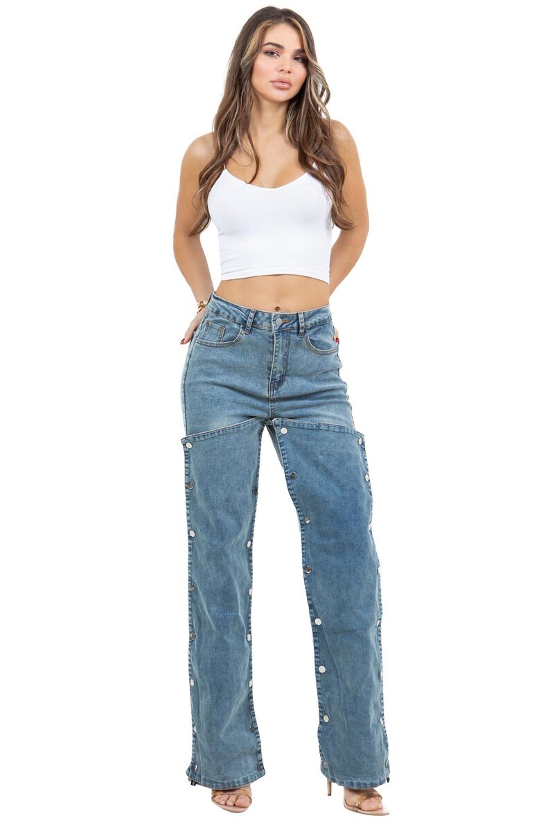 K&ouml;nnte beinhalten: Hellblaue Jeans mit Knopfdetails an den Au&szlig;enn&auml;hten. Die Jeans wird mit einem wei&szlig;en Crop-Top kombiniert. Das Model tr&auml;gt High Heels.