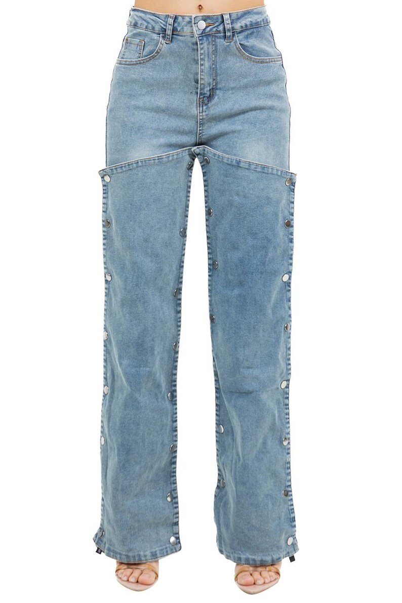 K&ouml;nnte beinhalten: Hellblaue Jeans mit einem einzigartigen Design. Die Jeans haben eine hohe Taille, einen Knopfverschluss und ein markantes Ausschnittdetail auf der Vorderseite. Silberfarbene Kn&ouml;pfe verlaufen entlang der &auml;u&szlig;eren N&auml;hte der Beine. Die Jeans sind aus hellem Denim.