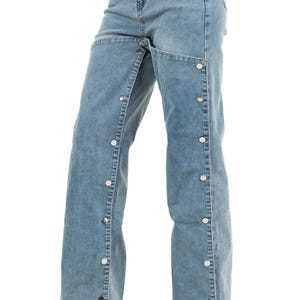 K&ouml;nnte beinhalten: Hellblaue Jeans mit einem einzigartigen Design. Die Jeans haben ein weites Bein und eine Reihe silberfarbener Kn&ouml;pfe entlang der Au&szlig;enn&auml;hte. Der Bund ist ein Standarddesign.