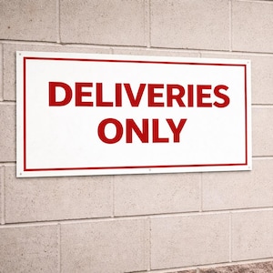 Może przedstawiać: Biały prostokątny znak z czerwonym napisem „DELIVERIES ONLY” jest zamontowany na ceglanej ścianie. W pobliżu zaparkowana jest ciężarówka dostawcza, z widocznymi w środku pudełkami. Obecny jest również pomarańczowy pachołek drogowy.