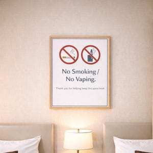 Könnte beinhalten: Ein Hotelzimmer mit zwei Betten, weißer Bettwäsche und braunen Kissen. Ein Nachttisch mit Lampe, Uhr und Telefon. Ein gerahmtes Schild an der Wand mit der Aufschrift "No Smoking / No Vaping."