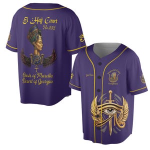 Könnte beinhalten: Lila Baseball-Trikot mit goldfarbenen Zierleisten und schwarzen Knöpfen. Die Vorderseite zeigt ein Augendesign mit Flügeln und einem Schwert. Die Rückseite zeigt Text und ein Bild einer Frau mit Kopfschmuck. Der Text enthält "El Hajj Court No. 252" und "Oasis of Musella Desert of Georgia."