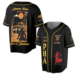 Könnte beinhalten: Schwarzes Baseball-Trikot mit gelben Zierleisten und Knöpfen. Das Trikot zeigt den Text "Ramadan Temple" und "PHA" in Gold. Auf der Rückseite des Trikots befindet sich eine Illustration einer Figur mit einem Schwert vor einem Gebäude und dem Text "Dasis of Southaven Desert of Mississippi".