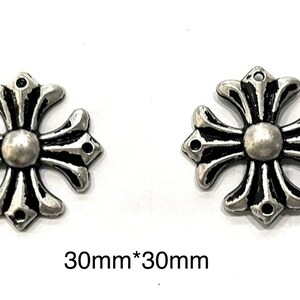 Op de afbeelding: Twee zilverkleurige kruisvormige bedels, elk met een centrale bol en sierlijke armen. De bedels zijn ongeveer 3 cm x 3 cm groot. Het ontwerp heeft een gedetailleerde, vintage esthetiek.