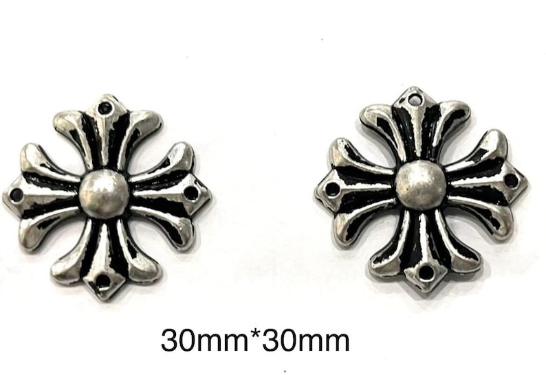 Op de afbeelding: Twee zilverkleurige kruisvormige bedels, elk met een centrale bol en sierlijke armen. De bedels zijn ongeveer 3 cm x 3 cm groot. Het ontwerp heeft een gedetailleerde, vintage esthetiek.