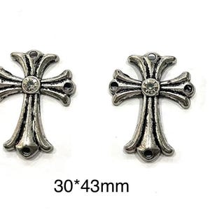 Op de afbeelding: Twee zilverkleurige kruisbedels met een decoratief ontwerp en een centrale heldere strass-steen. Elk kruis heeft een lus aan de boven- en onderkant om aan sieraden te bevestigen. Tekst: "30*43mm".