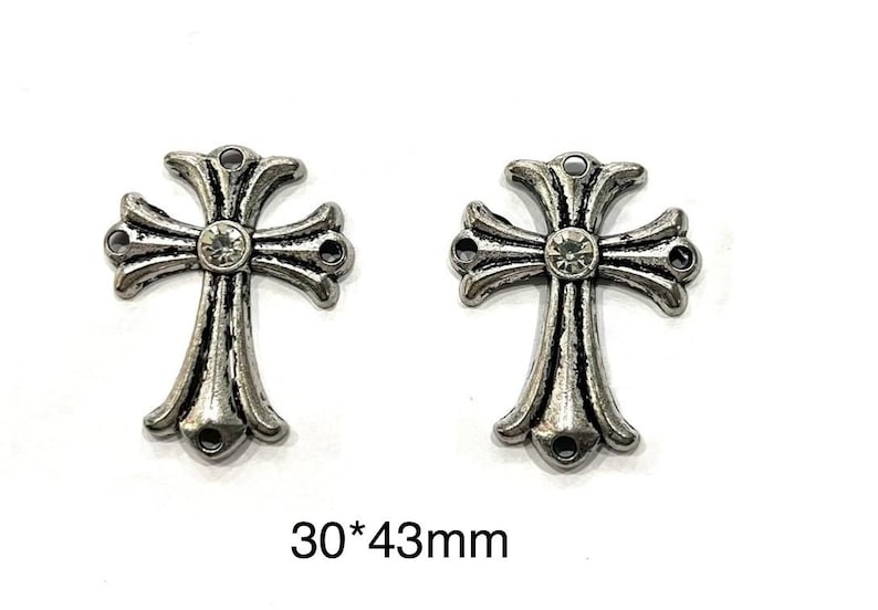 Op de afbeelding: Twee zilverkleurige kruisbedels met een decoratief ontwerp en een centrale heldere strass-steen. Elk kruis heeft een lus aan de boven- en onderkant om aan sieraden te bevestigen. Tekst: "30*43mm".