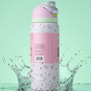 May include: A white Owala water bottle featuring a pink and blue floral pattern, a light green collar, and a grey lid with a push-button mechanism. The bottle has a pink product label wrapped around the centre with printed text and a barcode.