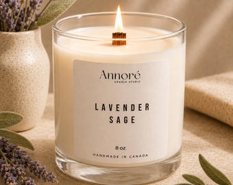 Op de afbeelding: Een kaars in helder glas met een houten lont en een wit etiket met de tekst Annoré Candle Studio, Lavender Sage, 8 oz, Handmade in Canada. De kaars bevat gebroken witte was en brandt met een kleine vlam in het midden van de houder.
