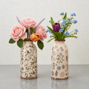 Può includere: Due vasi decorativi pieni di fiori. Il vaso a sinistra ha un motivo floreale e contiene rose rosa e un tulipano arancione. Il vaso a destra ha un design floreale e contiene un tulipano viola e fiori blu.