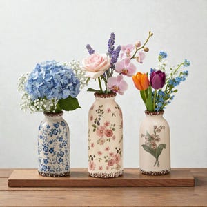 Peut inclure: Trois vases en céramique décoratifs avec des motifs floraux et des bordures marron, chacun contenant un arrangement de fleurs fraîches. Les vases sont présentés sur un plateau en bois, mettant en valeur une variété de couleurs et de textures.