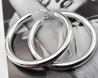 May include: A pair of silver hoop earrings. The earrings are a thick, rounded design with a polished finish. They are shown against a monochrome background.