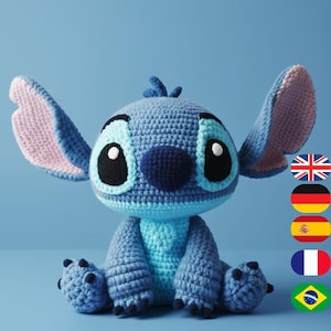 May include: A handmade crochet Stitch doll in shades of blue, with large ears, black eyes, and a dark blue nose. The plush toy is sitting on a light blue surface, showcasing its detailed craftsmanship and soft texture.