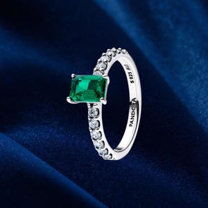 Op de afbeelding: Zilveren ring met een rechthoekige, smaragdgroene edelsteen. De band is versierd met kleine, heldere edelstenen. De ring is gemarkeerd met "S 925 ALE" en "PANDORA".