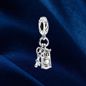 Może przedstawiać: Srebrny charms przedstawiający klucz i drzwi z twarzą. Charms wisi na pętli z wygrawerowanym napisem "Pandora" i "ALE S925". Ten charms jest przeznaczony do bransoletki.