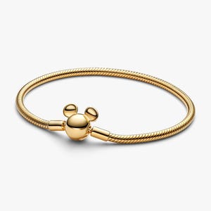 May include: A gold-toned snake chain bracelet featuring a polished, spherical clasp shaped like a stylized mouse head with two rounded ears. The bracelet has a flexible, textured metal band that forms a circular shape, showcasing a smooth, reflective finish throughout the entire piece.