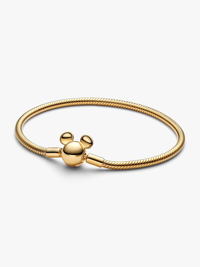 May include: A gold-toned snake chain bracelet featuring a polished, spherical clasp shaped like a stylized mouse head with two rounded ears. The bracelet has a flexible, textured metal band that forms a circular shape, showcasing a smooth, reflective finish throughout the entire piece.