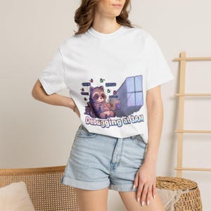 May include: White t-shirt with a cartoon raccoon engrossed in laptop work, text reads "Debugging at 3AM". The design includes computer bugs in purple, blue, and brown. A fun, tech-themed graphic.