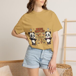 Peut inclure: T-shirt jaune moutarde avec un dessin animé de deux pandas avec des points d'interrogation. Le texte "MERGE CONFLICT" est au-dessus des pandas, avec des flèches et des symboles de code. Le t-shirt est porté par une personne.