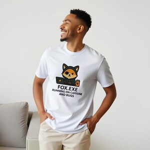 May include: White t-shirt with a cartoon fox graphic wearing a hoodie and using a laptop. The text "FOX.EXE RUNNING ON CAFFEINE AND BUGS" is printed below the fox illustration. The shirt is made of a soft material.
