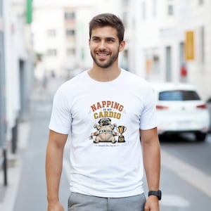 Peut inclure: T-shirt blanc avec un motif de bouledogue tenant un trophée et le texte "Napping is my Cardio". Le design comprend les mots "Finish" et "Champion Since Day One". Le t-shirt est porté par une personne.