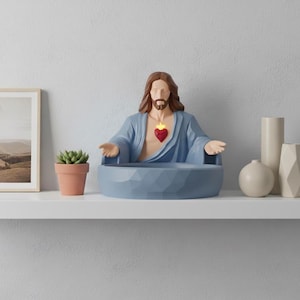 May include: A decorative shelf displays a framed landscape print, a small potted succulent, and a blue Jesus figure with a heart-shaped emblem. Additional decor includes vases, books, and a candle.