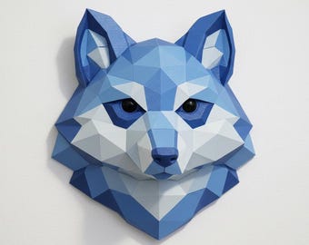 May include: A geometric, low-poly style fox head wall decor in shades of blue and white. The artwork features a detailed, angular design with black eyes and a pointed nose, mounted on a white wall. This piece is a modern take on animal art.