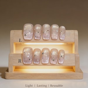 Könnte beinhalten: Ein Set hellrosa Press-On-Nägel mit Glitzer und Sternen-Designs, präsentiert auf einem Holzständer. Der Text unten lautet "Light | Lasting | Reusable". Die Nägel sind mit "L" und "R" beschriftet.