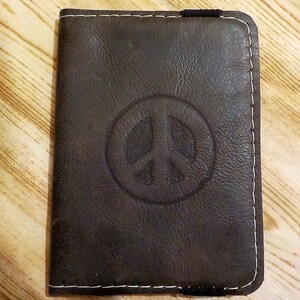 May include: A brown leather wallet with a white peace sign embossed on the front.