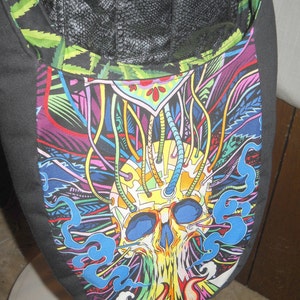 May include: A black fabric bag with a colorful skull design. The skull is surrounded by colorful lines and swirls. The bag has a black leather flap at the top.