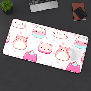 May include: A white rectangular mousepad featuring a repeating pattern of cartoon cat faces in pink, white, and light blue. The cats have smiling faces and are interspersed with pink hearts and stars. A white mouse sits on the pad.