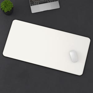 May include: A white rectangular desk mat with a black border, a white computer mouse, and a small potted plant are on a dark gray surface. A laptop is partially visible in the background.