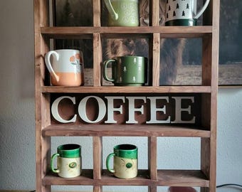 May include: A wooden coffee mug display shelf with various mugs. The mugs have different designs, including trees, flowers, and a rainbow. The word "COFFEE" is displayed on the shelf. The shelf is made of dark brown wood.