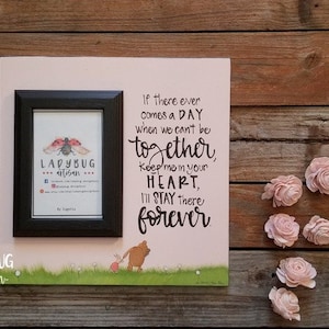 May include: A pink wooden sign with a black frame and a quote that reads "If there ever comes a DAY when we can't be together, Keep me in your HEART, I'll STAY there forever". The sign also features a small picture frame with a ladybug illustration and the text "LADYBUG artisan".