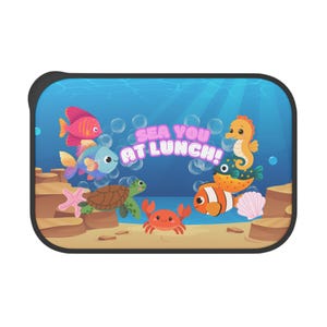 以下が含まれることがあります： ピンク、オレンジ、青の魚、ウミガメ、カニ、タツノオトシゴ、カクレクマノミが描かれた青い海中の風景の長方形のサンシェード。中央にはSEA YOU AT LUNCH!という文字がプリントされており、周囲には泡が描かれています。