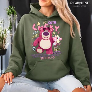A person wearing a green hoodie with a cartoon bear design and text printed on it.