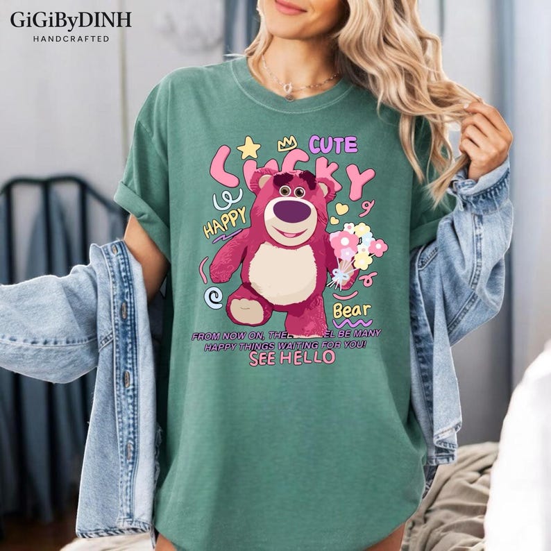 A woman wearing a green t-shirt with a cartoon bear graphic and text, including the words "Cute", "Happy", "From now on, the bear is waiting for you to see hello".